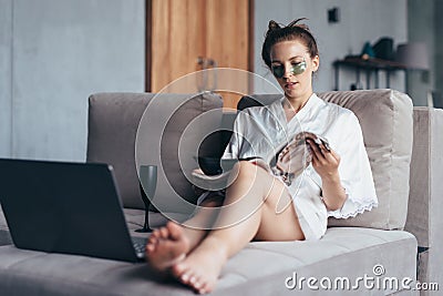 Young woman sitting at home with face beauty mask and reading magazine Stock Photo