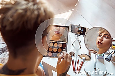 Make-up Tutorial. Young woman sitting watching video on smartphone applying eyeshadow smiling joyful close-up Stock Photo