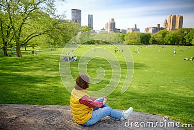 Young woman sitting on large stone in Central Park in New York on sunny spring day. Sheep meadows are lovely place for rest, relax Stock Photo