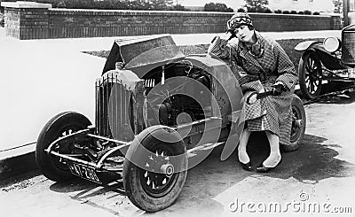 Young woman sitting next to small car looking at the engine in disbelieve Stock Photo