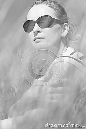 Young woman sitting in sand dunes amongst tall grass relaxing, enjoying the view on sunny day Stock Photo