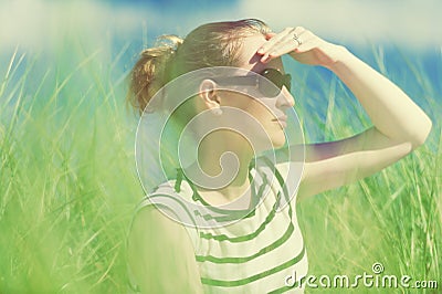 Young woman sitting in sand dunes amongst tall grass relaxing, enjoying the view on sunny day Stock Photo