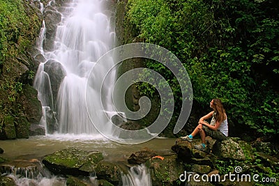 Young woman sitting at Simangande falls on Samosir island, Sumatra, Indonesia Stock Photo