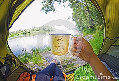 Young woman sitting in the tent and drinking tea while looking on the Desna river Stock Photo