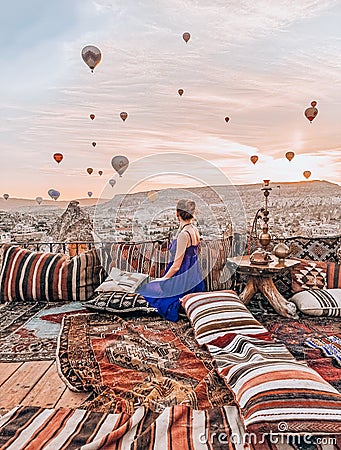 Young woman sitting on the terrace in Cappadocia watching sunrise and air balloons Stock Photo