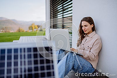 Young woman sitting on terrace, charging tablet trough solar panel. Stock Photo