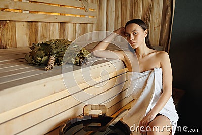 Young woman sitting on a wooden bench in a traditional sauna. Stock Photo