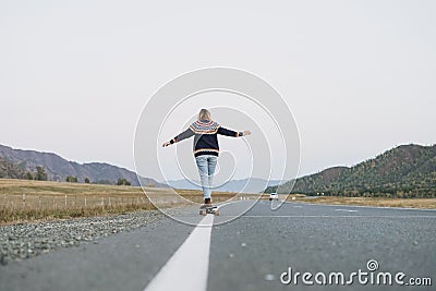 Young woman on skateboard on the road against beautiful mountain landscape, Chuysky tract, Altai Stock Photo