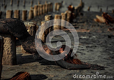 Young woman smeared with therapeutic mud and lies on wooden column. Stock Photo