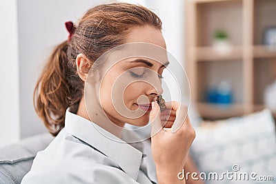 Young woman smelling marihuana bud sitting on sofa at home Stock Photo