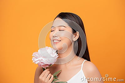 Young woman sniffing pink peony flower closed her eyes on yellow background Stock Photo