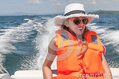 Young woman on a speed boat in a life jacket on a background foamy trace of the boat. Stock Photo