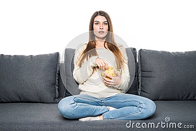 Young woman spends his free time watching TV on the couch at home, munching chips. Stock Photo