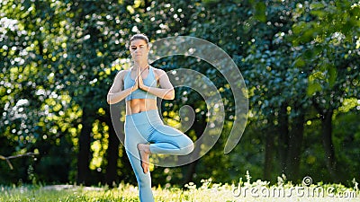 Young woman sportive trainer in blue tracksuit workouts standing in yoga tree pose Stock Photo