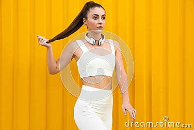 Young woman in sportswear with headphones near corrugated yellow metal wall Stock Photo
