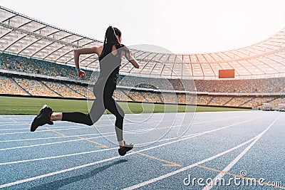 Young woman in sportswear sprinting on running track stadium at sunset Stock Photo