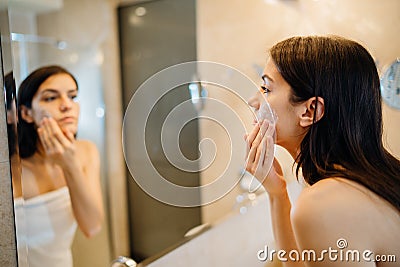 Young woman spreading hydration products,skincare routine at home.Daytime facial creme.Removing makeup.Spa day,having fun.Feminine Stock Photo