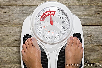 Young woman standing on classic analogue weight scale indicating overweight Stock Photo