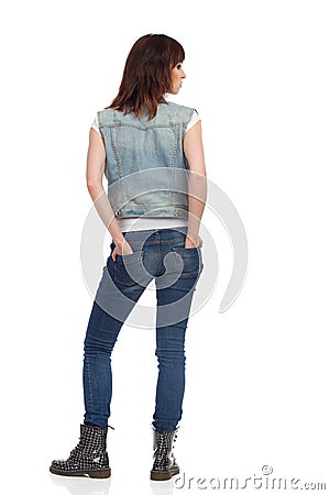 Young Woman Is Standing, Holding Hands In Pocket And Looking Away. Rear View. Stock Photo