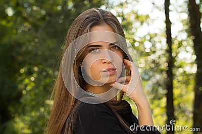 Young woman standing sidewise on the background of trees Stock Photo