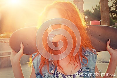 A young woman is standing in the street holding skateboard behind her head. Outdoors. Street fashion lifestyle. Stock Photo