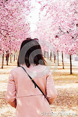 Young woman standing in a tranquil atmosphere surrounded by a canopy of delicate pink blossoms Stock Photo