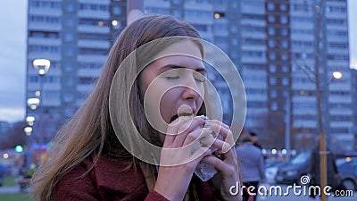 Young woman standing in an urban street and eating burger. Young woman eating fast food standing on the street Stock Photo