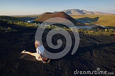 A young woman is standing in a yoga pose against the beautiful nature landscape of valley, volcanic lake and crater Stock Photo