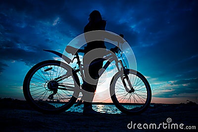 Young woman staying on the shore of the lake with bicycle at sun Stock Photo