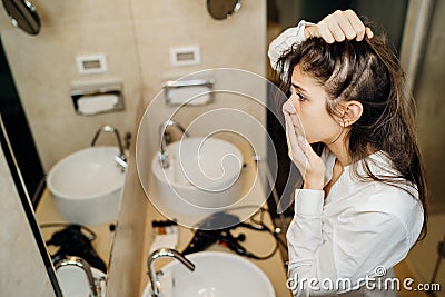 Young woman suffering from alopecia. Female hair loss.Worried female looking her hairline in the mirror.Stress caused problem, Stock Photo