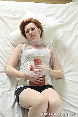 Young woman suffering stomach cramps on belly holding hot water bottle against tummy Stock Photo