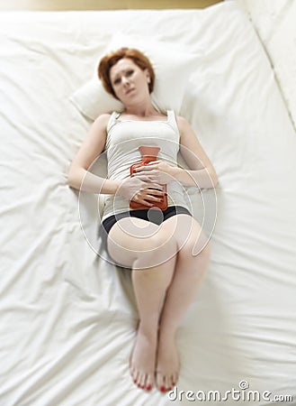 Young woman suffering stomach cramps on belly holding hot water bottle against tummy Stock Photo