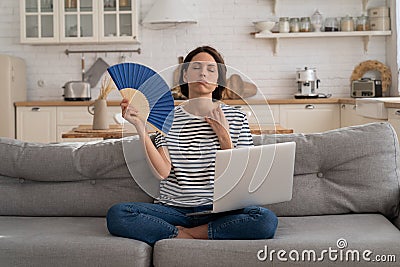 Young woman suffers from heatstroke flat without air-conditioner waving fan sitting on couch at home Stock Photo