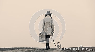 Young woman with suitcase and dog standing on the road Stock Photo