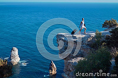 Young woman with suitcase and laptop going on sea rock. Travelling and remote work concept. Life work balance idea Stock Photo