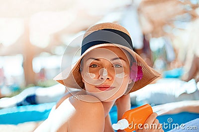 Young woman with sun cream on face holding sunscren bottle on the beach. Stock Photo