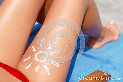 Young woman with sun shape on the leg holding sun cream bottle on the beach. Sun protection sun cream, on her smooth tanned legs.S Stock Photo