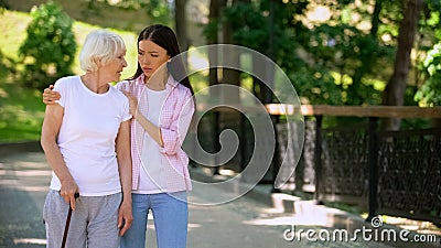 Young woman supporting sick aged lady walking stick, illness depression, rehab Stock Photo