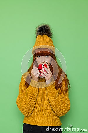 Young woman in sweater and cap with pompom is holding red mug Stock Photo