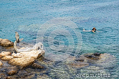 Happy young woman swimming in the sea near a sculpture, Summer holidays. Stock Photo