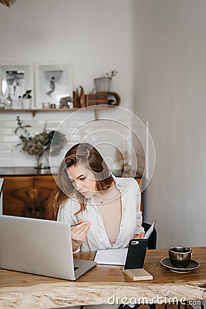 Young woman takes notes in front of laptop at home. Working from home. Concept of education and communication. Stock Photo