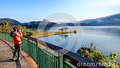 A young woman takes a photo of a beautiful natural scenery at Sun Moon Lake, Taiwan Editorial Stock Photo