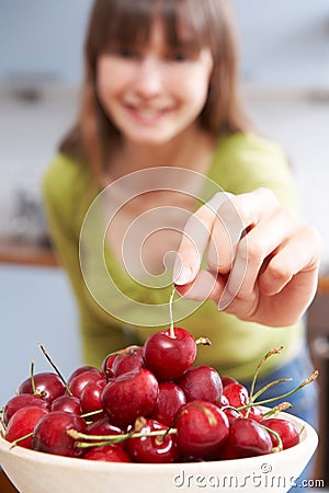 Young Woman Taking Cherry From Wooden Bowl Stock Photo