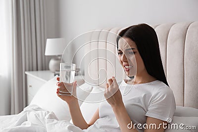 Young woman taking medication for migraine in bed at home Stock Photo