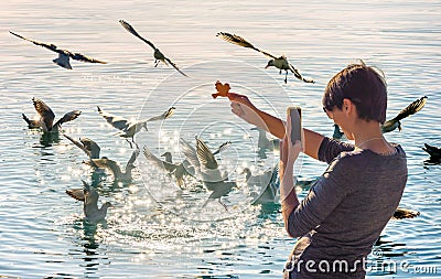 Young woman taking a picture with her phone of Flock of seagulls Stock Photo