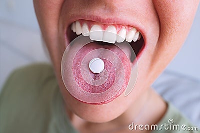 Young woman taking pill. Closeup of white round pill on tongue. Open mouth holding tablet Stock Photo