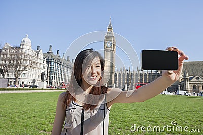 Young woman taking self portrait through smart phone against Big Ben at London, England, UK Stock Photo