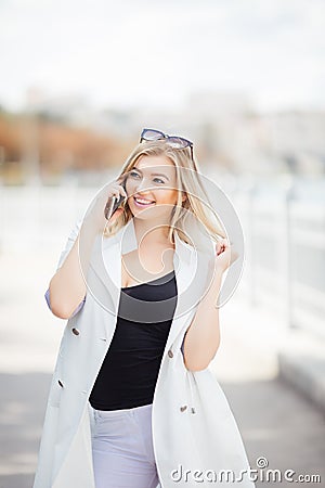 Young woman talking on her mobile phone listening to the conversation , she stands outdoors on granite embankment against a river Stock Photo