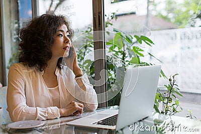 Young woman talking on mobile while sitting in a cafe with a laptop. Stock Photo