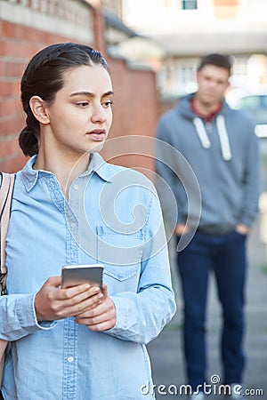 Young Woman Texting For Help On Mobile Phone Whilst Being Stalked On City Street Stock Photo
